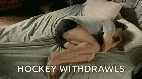 a man is laying on a bed with his legs crossed and the words `` hockey withdrawls '' above him .