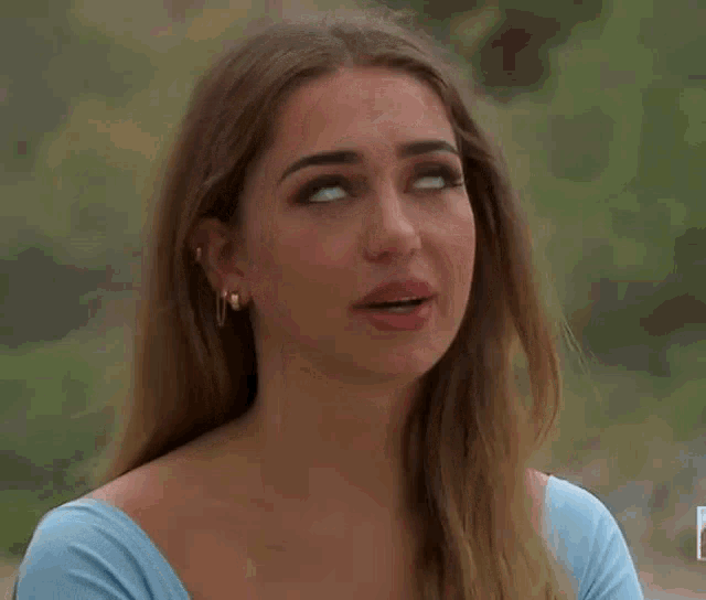 a close up of a woman wearing a blue shirt and earrings making a funny face .