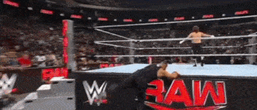two men are wrestling in a wrestling ring with a sign that says raw .