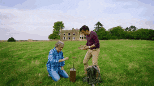 two men are kneeling in a grassy field in front of a building