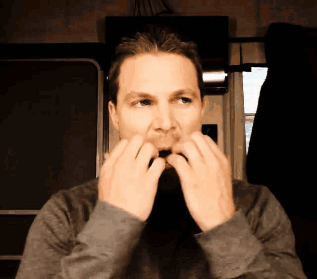 a man in a gray sweater holds his hands to his mouth