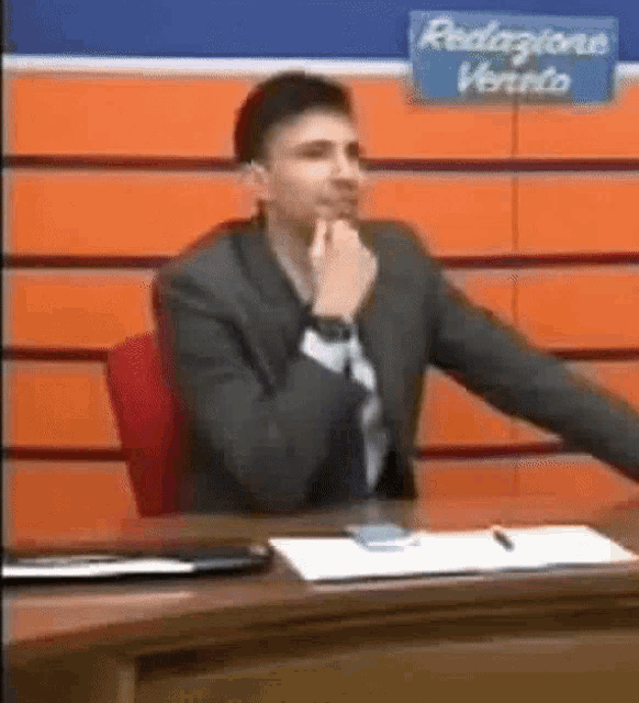 a man in a suit and tie is sitting at a desk in front of an orange wall .