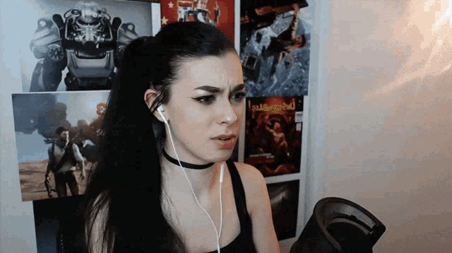 a woman wearing ear buds stands in front of a wall with pictures of fallout