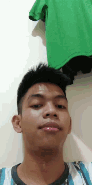a young man is taking a selfie with a green shirt hanging on the wall behind him