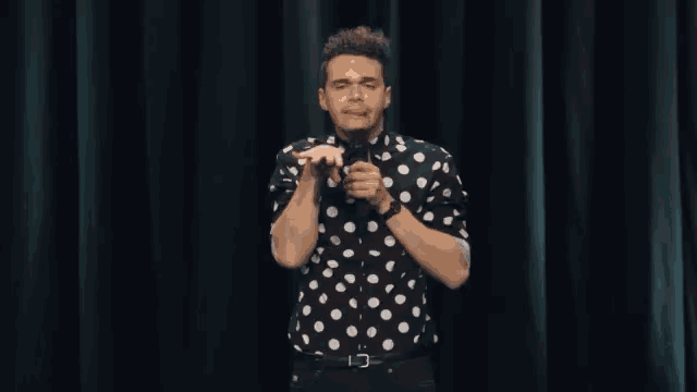 a man wearing a black and white polka dot shirt is holding a microphone