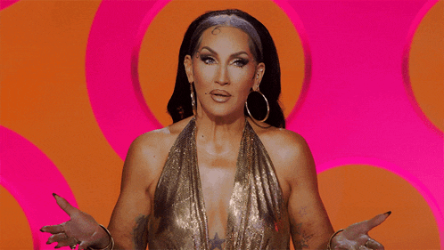 a woman wearing a gold top and hoop earrings is standing in front of a pink and orange background