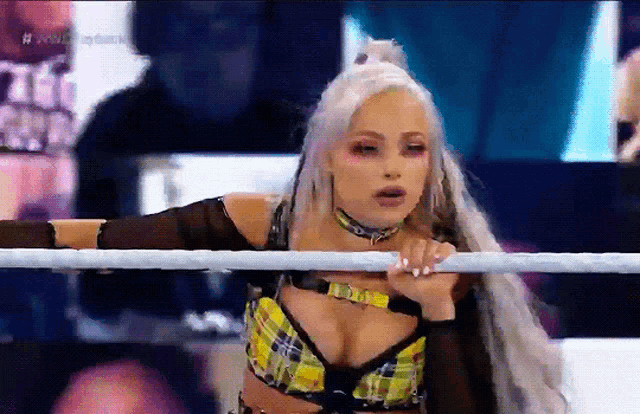 a woman in a plaid top is leaning on a rope in a ring .