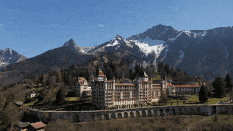 a large building sits on top of a hill surrounded by snow covered mountains