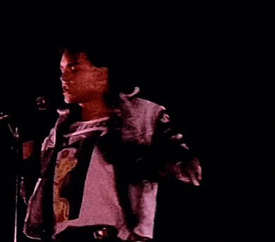 a man in a leather jacket is singing into a microphone in a dark room