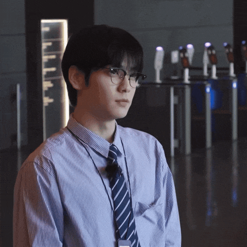 a man wearing glasses and a striped shirt stands in a hallway