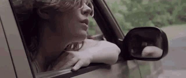 a woman is sitting in a car looking out the window .