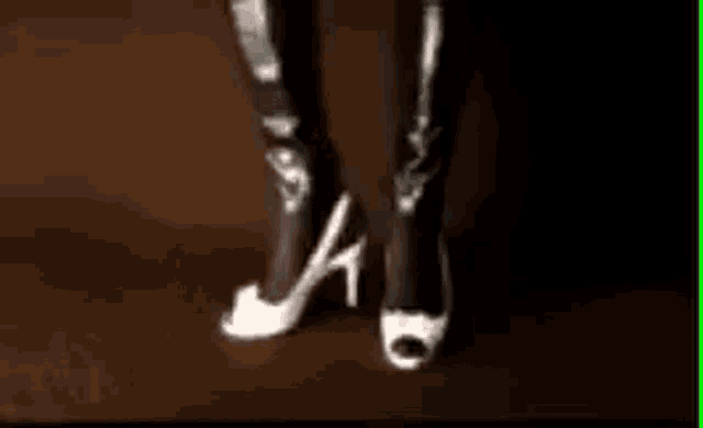 a woman is wearing a pair of white high heels and black leather pants .
