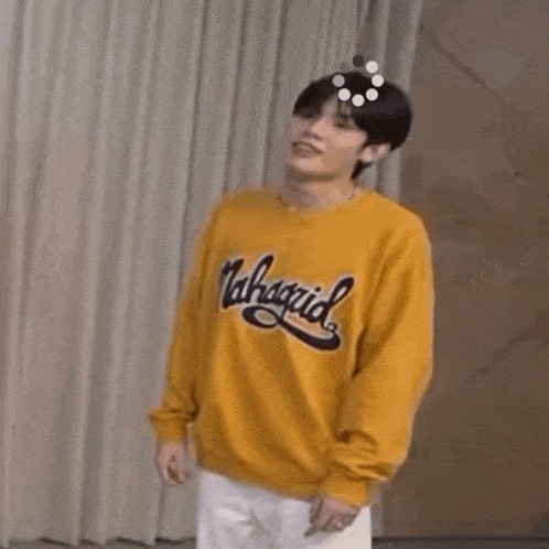 a young man wearing a yellow sweatshirt is standing in front of a curtain .