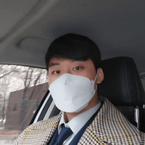 a man wearing a face mask and a plaid jacket is sitting in a car