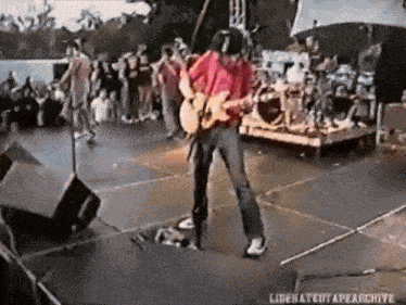 a man in a red shirt is playing a guitar on a stage in front of a crowd ..