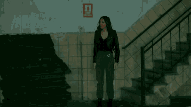 a woman in a black jacket and green pants walks down a set of stairs in front of a fire escape sign