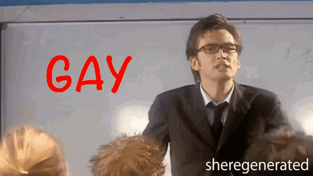 a man in a suit and tie stands in front of a whiteboard with the word gay written on it