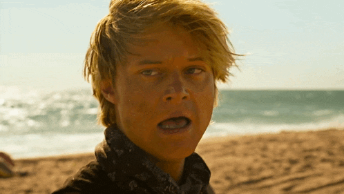 a close up of a man 's face on a beach with his mouth open