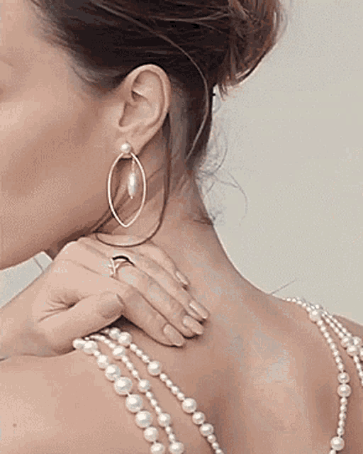 a woman wearing pearl earrings and a pearl necklace has her hand on her neck