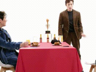 a man in a suit is standing next to a woman sitting at a table