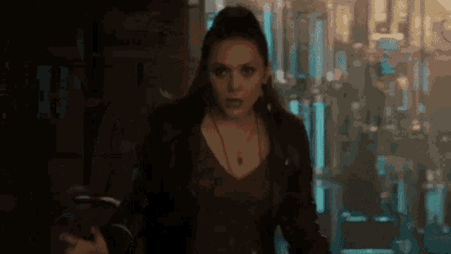 a woman in a red dress and black jacket is standing in a dark hallway .