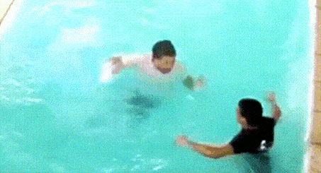 a man in a white shirt is swimming in a pool while a woman watches .
