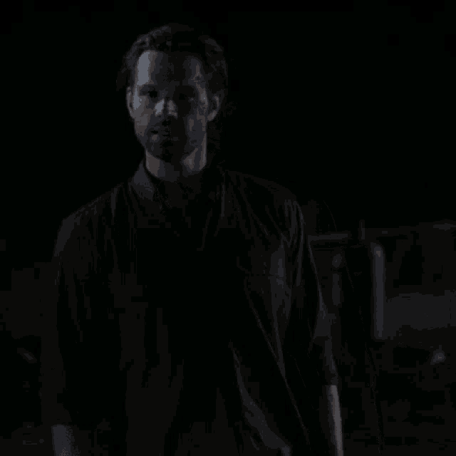 a man in a black shirt and tie stands in the dark