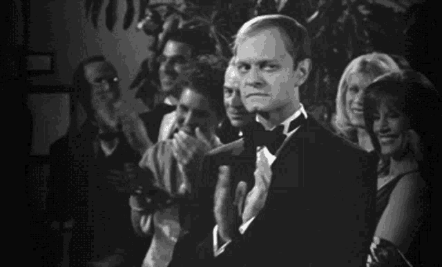 a man in a tuxedo is clapping his hands in a black and white photo