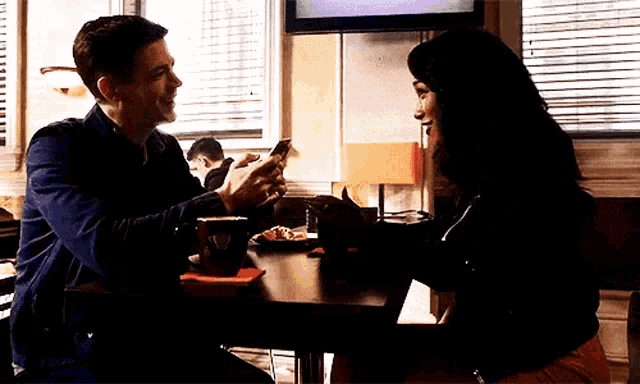 a man and a woman are sitting at a table in a restaurant looking at their cell phones .