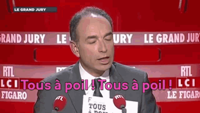 a man in a suit and tie is speaking into a microphone while holding a sign that says tous a poil