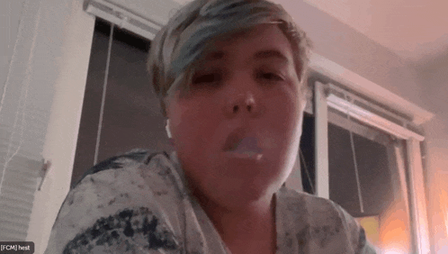a woman smoking a cigarette in front of a window with a screen that says jfcm heist on it
