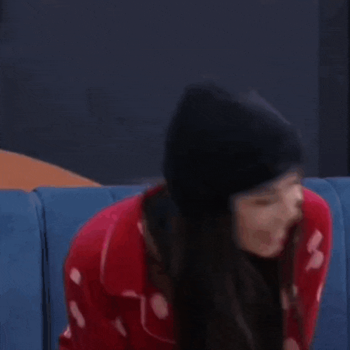 a woman wearing a black beanie and a red sweater with hearts is sitting on a blue couch .