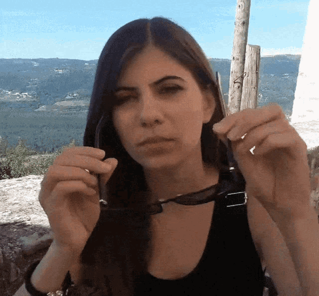 a woman wearing sunglasses looks at the camera with a mountain in the background