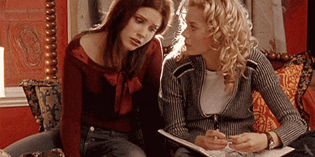 two women are sitting next to each other on a couch looking at a piece of paper .