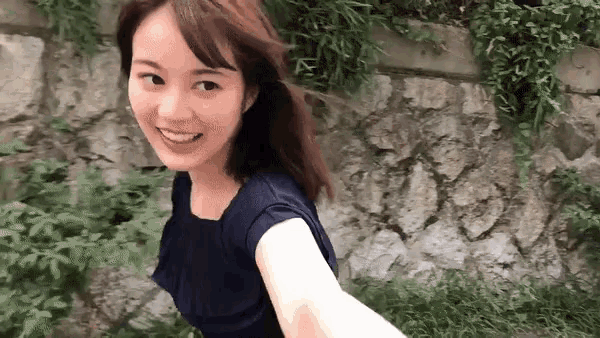 a woman in a blue shirt is smiling in front of a rock wall