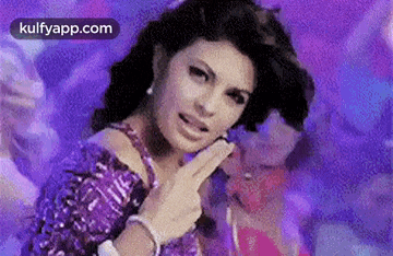 a woman in a purple dress is making a funny face and pointing at the camera .