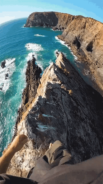 a person is sitting on a rocky cliff overlooking the ocean