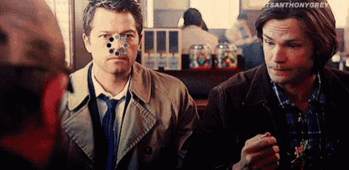 two men are standing next to each other in a restaurant . one of the men has a sticker on his nose .