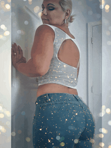 a woman in a white tank top and blue jeans is leaning against a door
