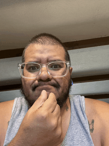 a man wearing glasses and a grey tank top has a tattoo on his arm