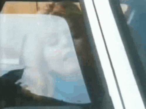 a person is sitting in a car with their eyes closed and looking out the window .