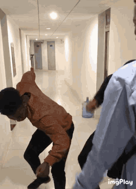 a man is dancing in a hallway with a bottle of water in the background