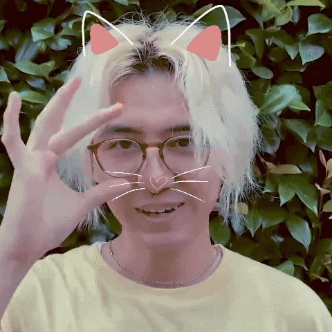 a man wearing glasses and a yellow shirt has a cat face drawn on his forehead