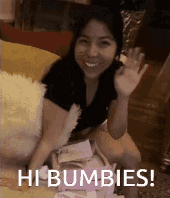a woman is sitting on a couch waving her hand and the words hi bubbies are below her