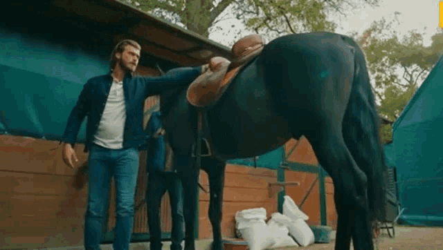 a man is standing next to a horse that has a saddle on it .