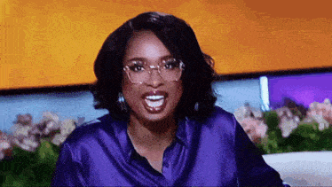 a woman wearing glasses and a purple shirt is smiling with her mouth open