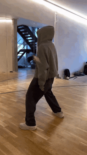 a person in a hoodie is walking on a wood floor
