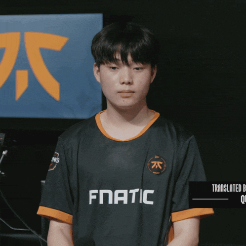 a young man wearing a fnatic jersey stands in front of a blue and orange sign