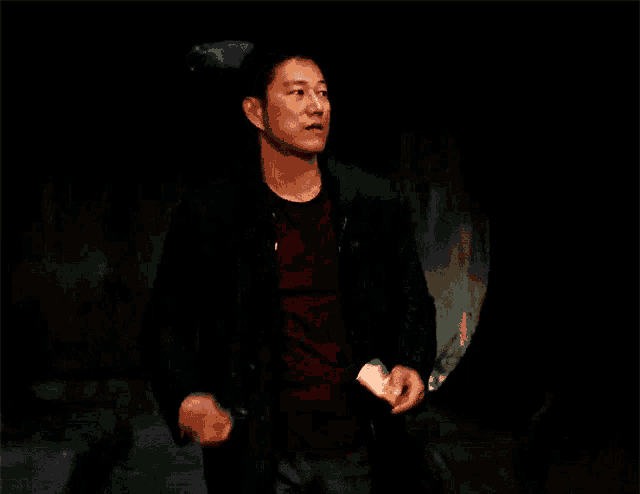a man in a black coat is standing in a dark room with his fist in the air