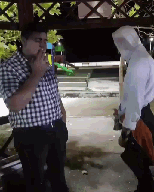 a man in a plaid shirt is smoking a cigarette next to another man in a white hoodie